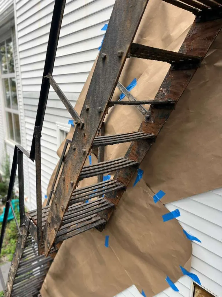 Before exterior metal stair restoration showing rust and preparation masking